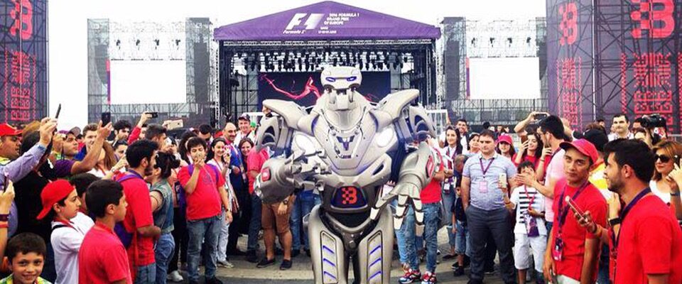 Titan the robot performs his show in front of a formula one stage, surrounded by a crowd