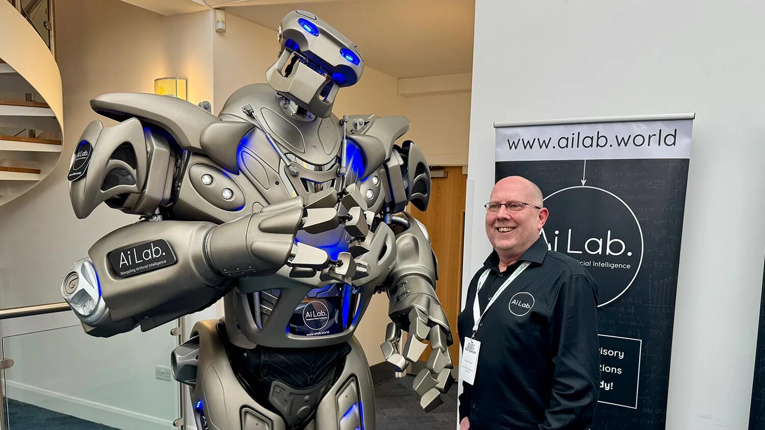 Titan the Robot stands next to the owner of AI labs, with AI labs branding panels on.