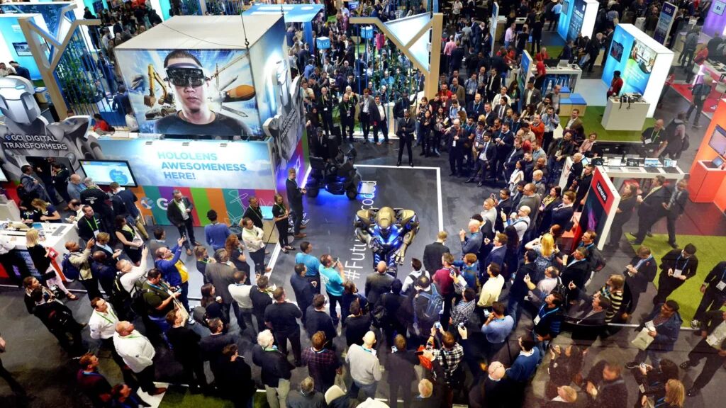 Titan stands next to a trade show stand that has his image on it. A large crowd has gathered in a circle to watch