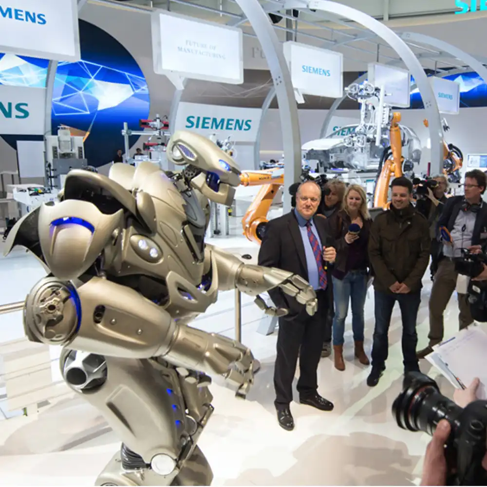 Titan the Robot stands in front of a car assembly line that has been setup as part of the Siemens stand at a trade show.
