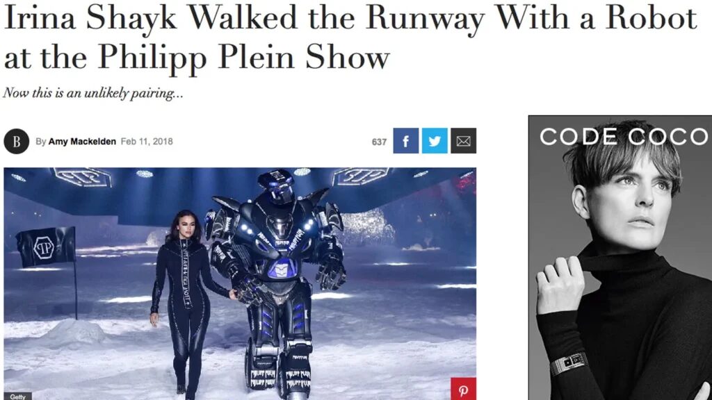 A web article. headline "Irina Shayk walked the runway with a robot at the philipp plein show". A black Titan the Robot walks on a snow covered catwalk with supermodel Irina Shayk wearing a black catsuit