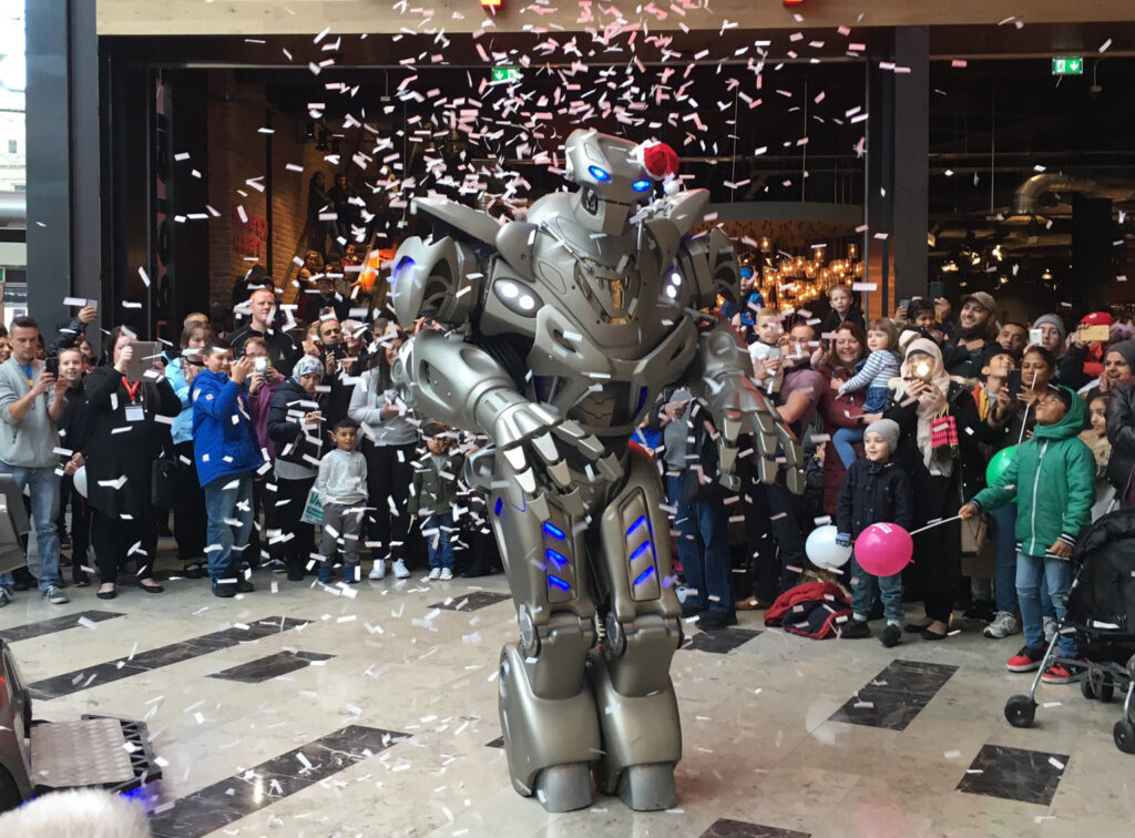 Titan the Robot stands under a wave of confetti, while singing a Christmas song